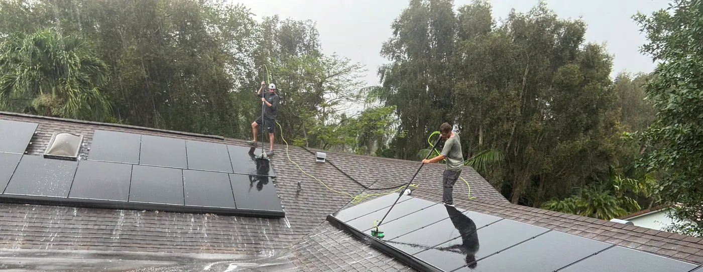 Two Luxsolis technicians washing rooftop solar panels with water-fed poles